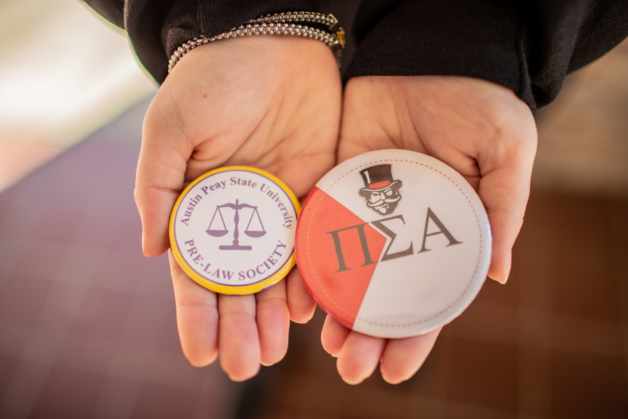 two button pins resting in Isabelle's hands. One is for Pre-Law Society and the other has Pi Sigma Alpha's Greek letters