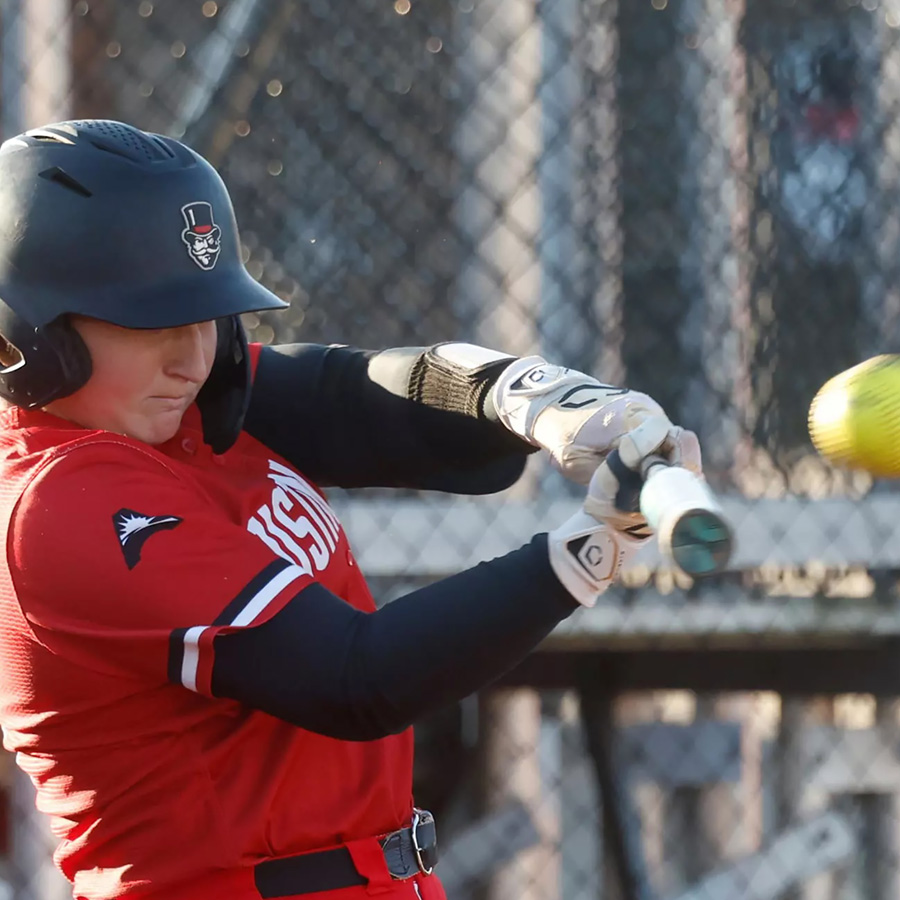 Softball player swinging the bat to hit the ball flying at her.
