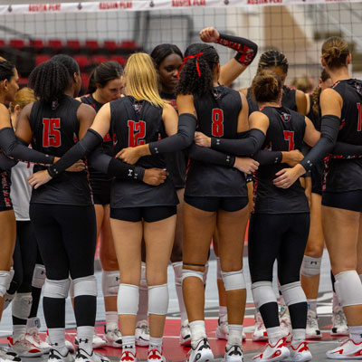The Governors Women's Volleyball team standing in a team huddle with their arms crossed over each others backs.