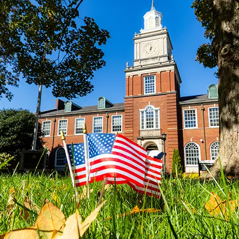 Picture of 3 small American flags planted in the Browning Quad grass with the Browning building behind them.