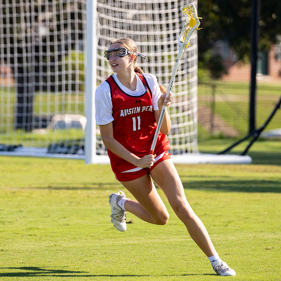 A Women's Lacrosse athlete catching the ball in the stick pocket and running across the field.