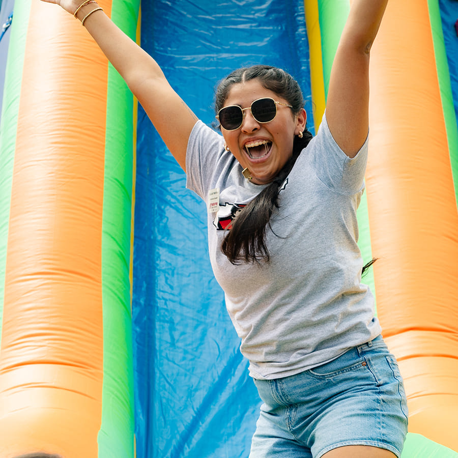 Young woman with her arms up in the air and cheering after coming down a bouncy slide.