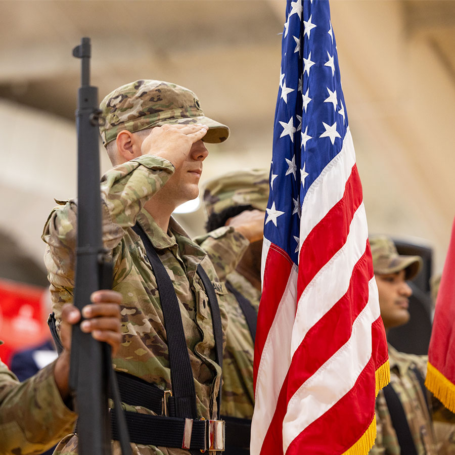 Soldier in uniform saluting next to an American flag.