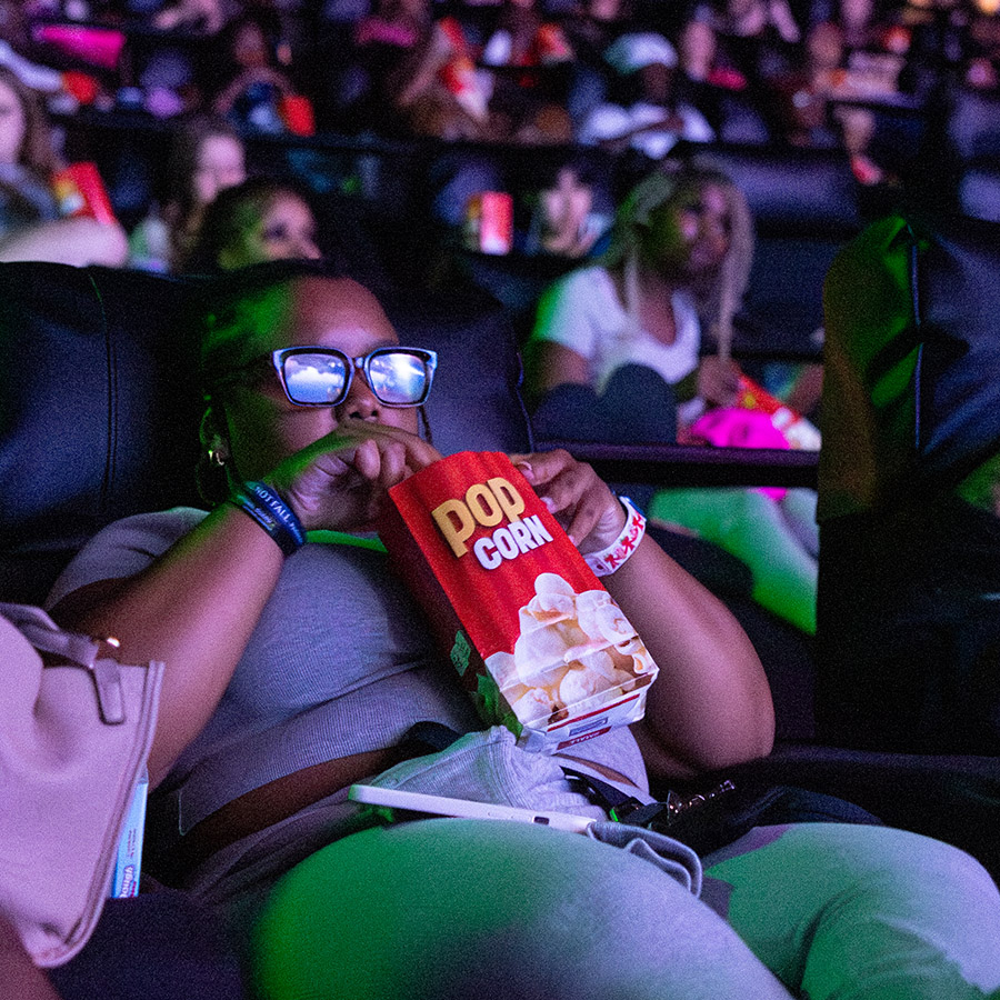 Student eating popcorn and watching the screen in a dark movie theater.