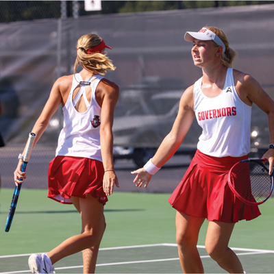 Two womens tennis players giving each other a low five as they run across the court
