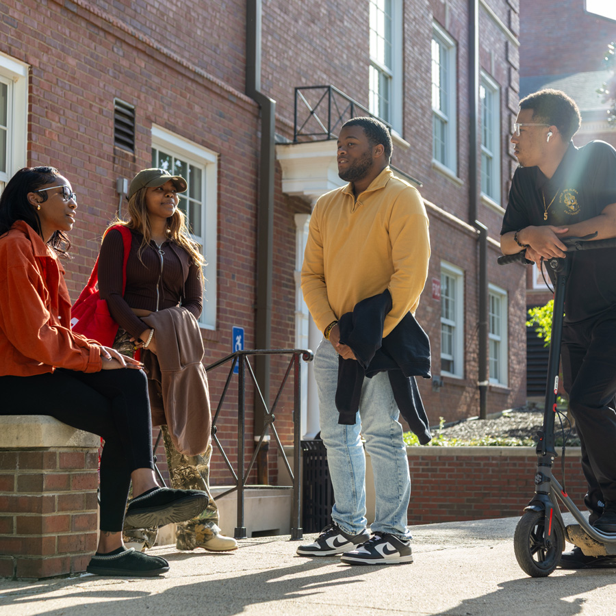 A group of four students hanging out on campus in the sunshine.