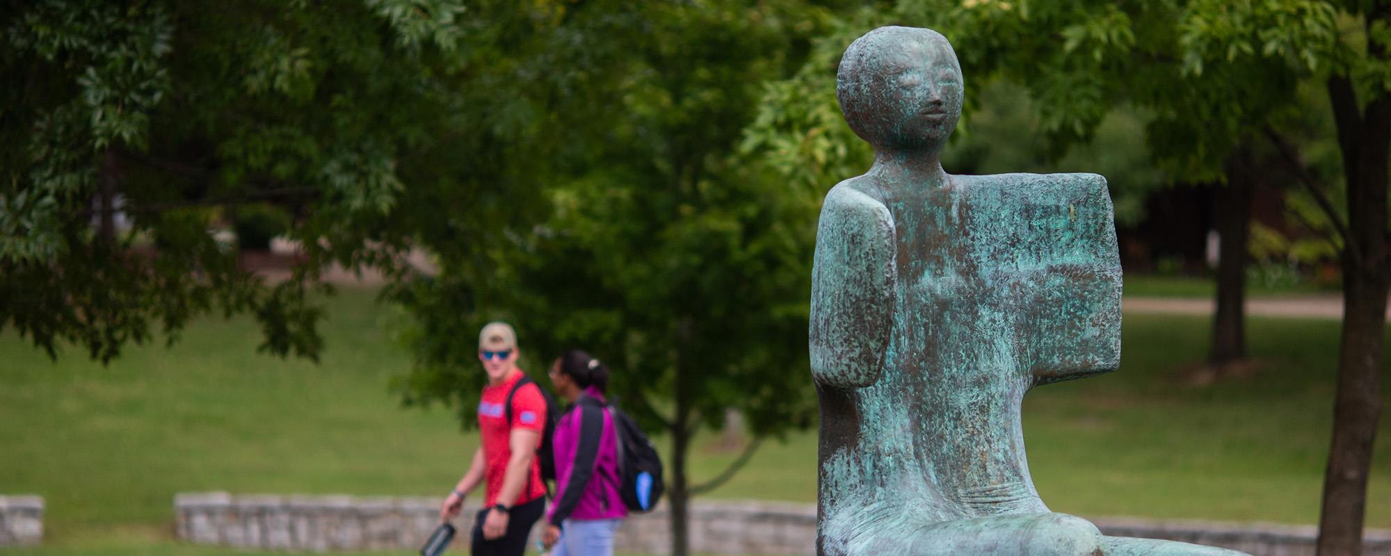 Green man sits with students walking behind