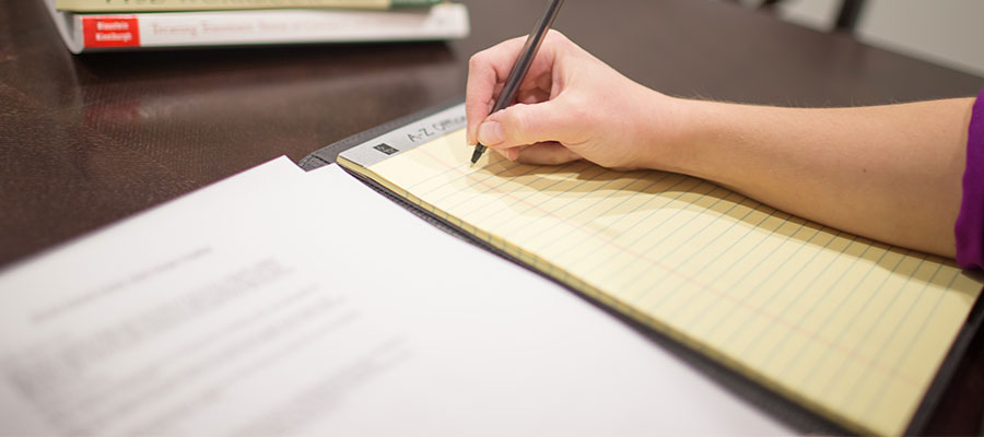 Hand holding a pen, planning to write on a yellow legal pad notebook.