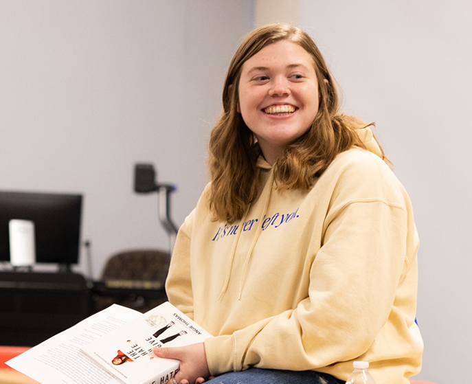 Mollie Scruggs smiling and holding a book during a bookclub meeting.