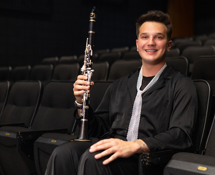Tyler Rose sitting in a theater seat holding his clarinet.