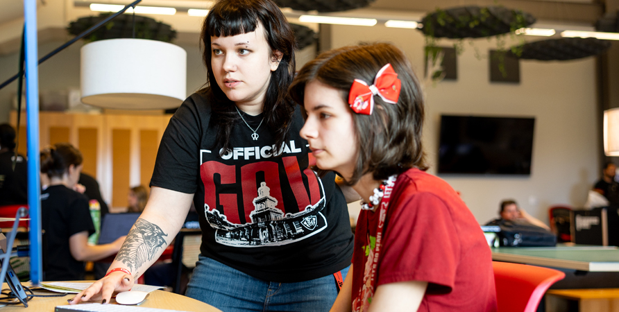 A current student helping a newer student with registration on a computer.