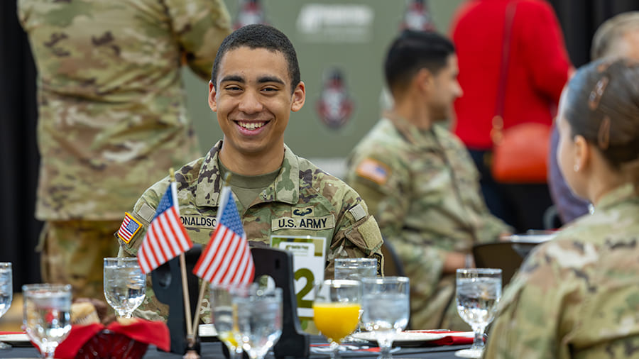 Student in Army uniform smiling while sitting at a table during a breakfast with other people in uniform.