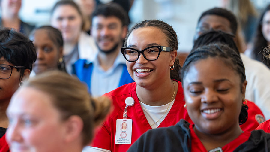 A crowd of students seated during a talk with the focus on a single female student smiling while listening to the speaker.