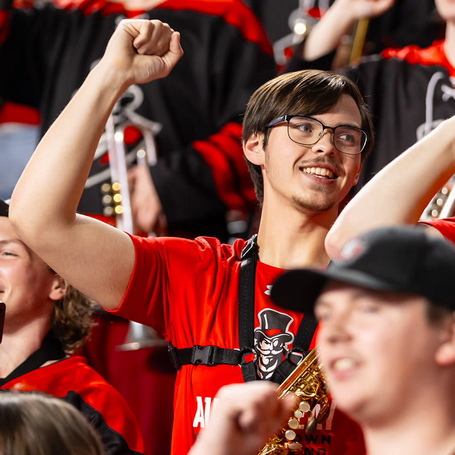 A student in the APSU Band among a crowd of his bandmates, pumping his fist in the air.