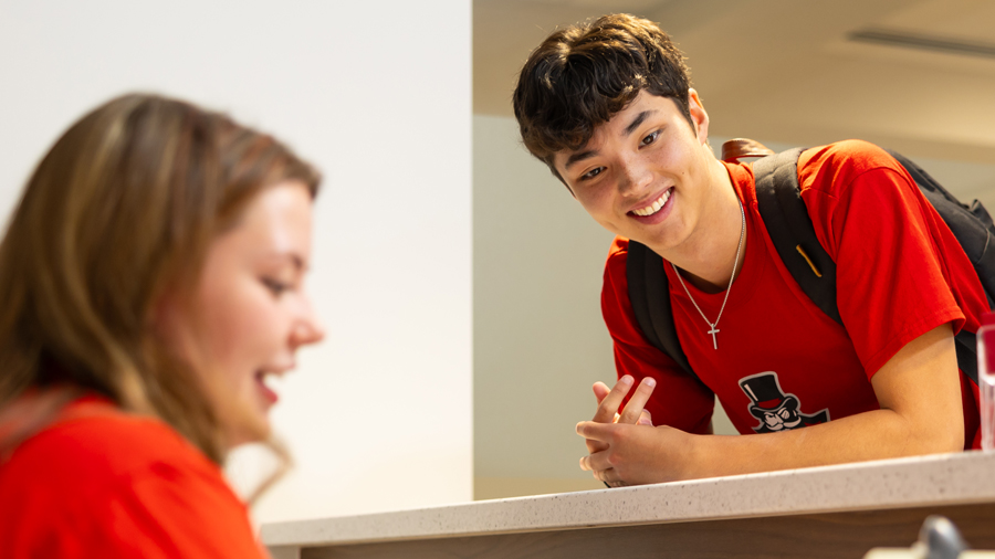 Student leaning on counter to speak with employee behind the desk.