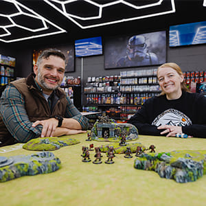 Anthongy and his partner in their Game store sitting at a table with game pieces spread out in front of them.