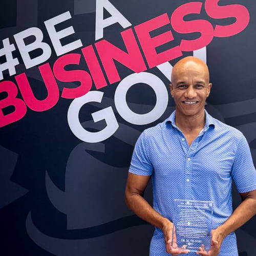 Dr. Al Tilooby holding his award in front of a backdrop that reads "#Be A Business Gov."