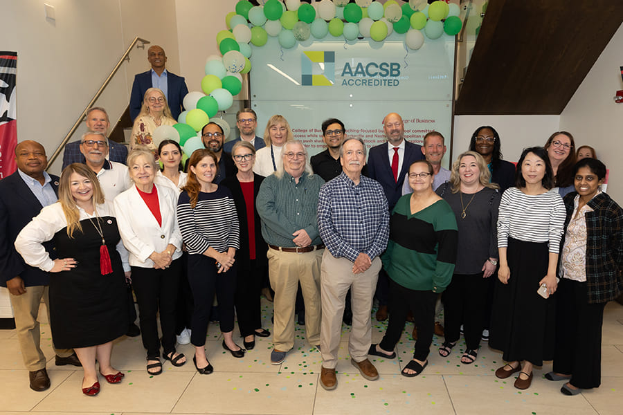 Group of people posing under a green and white balloon arch in front of an AACSB Accredited sign.