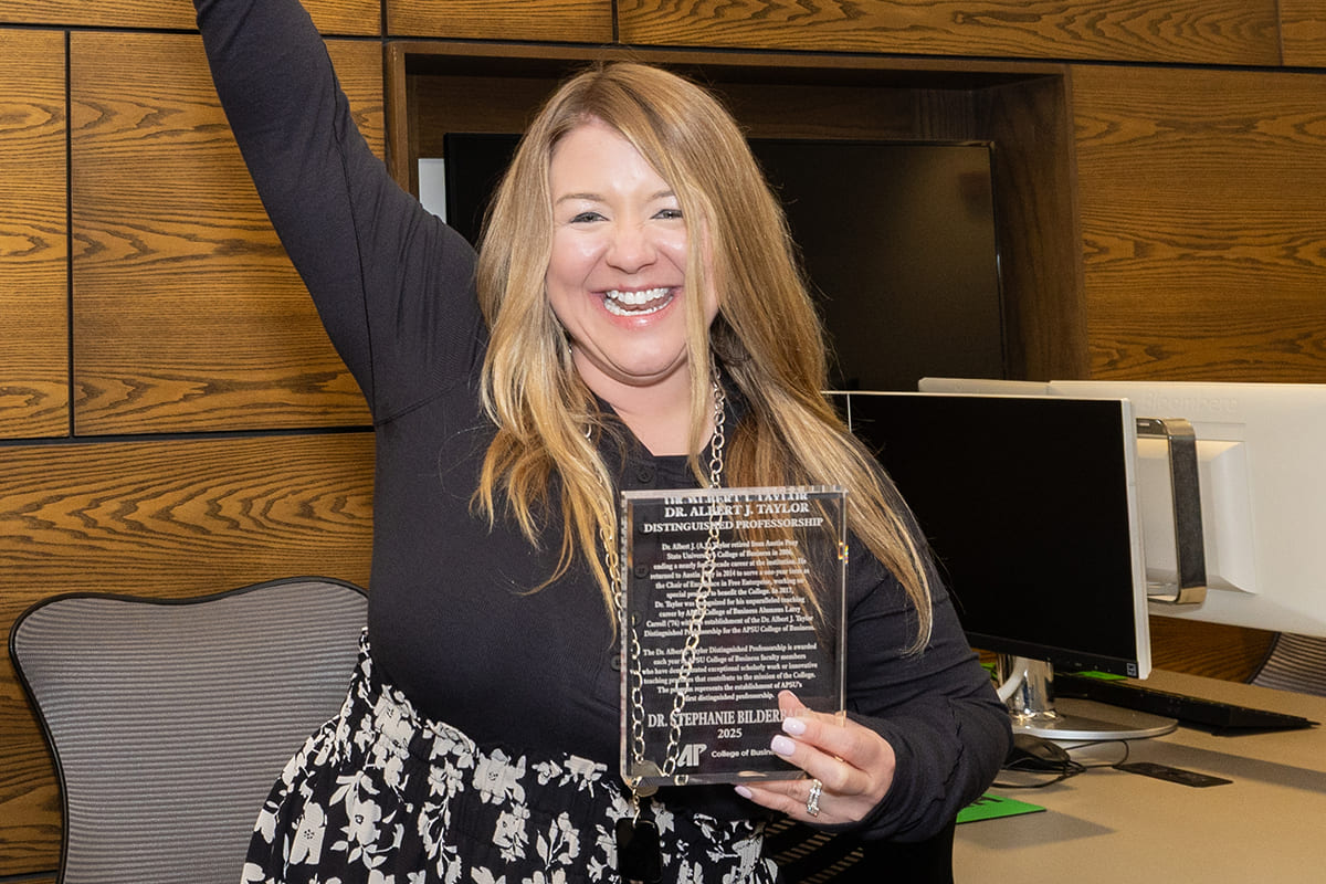Dr. Bilderback holding her award and cheering with a huge smile and her arm up in the air.