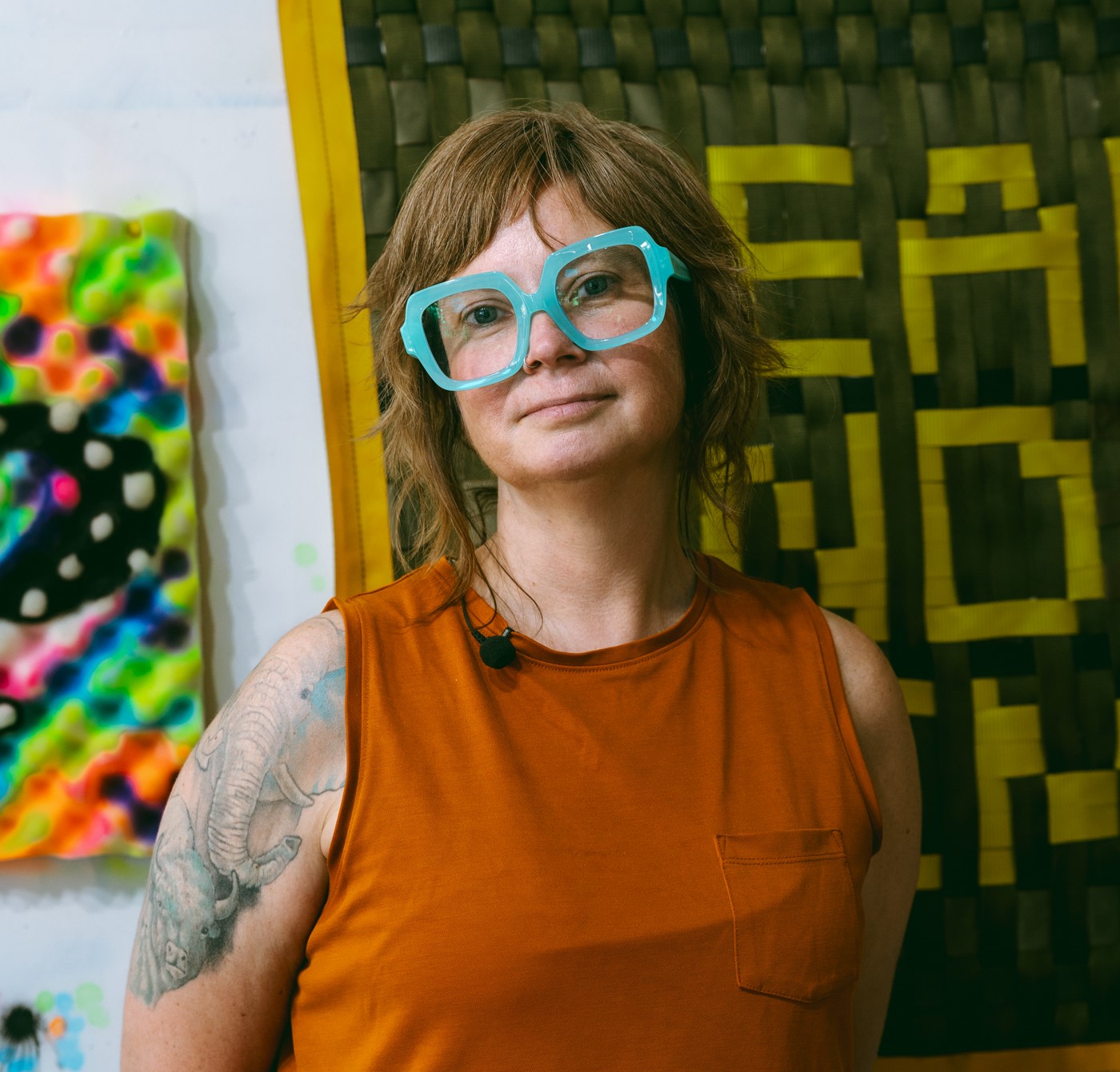 Briena Harmening head shot wearing blue glasses against background of textile art.
