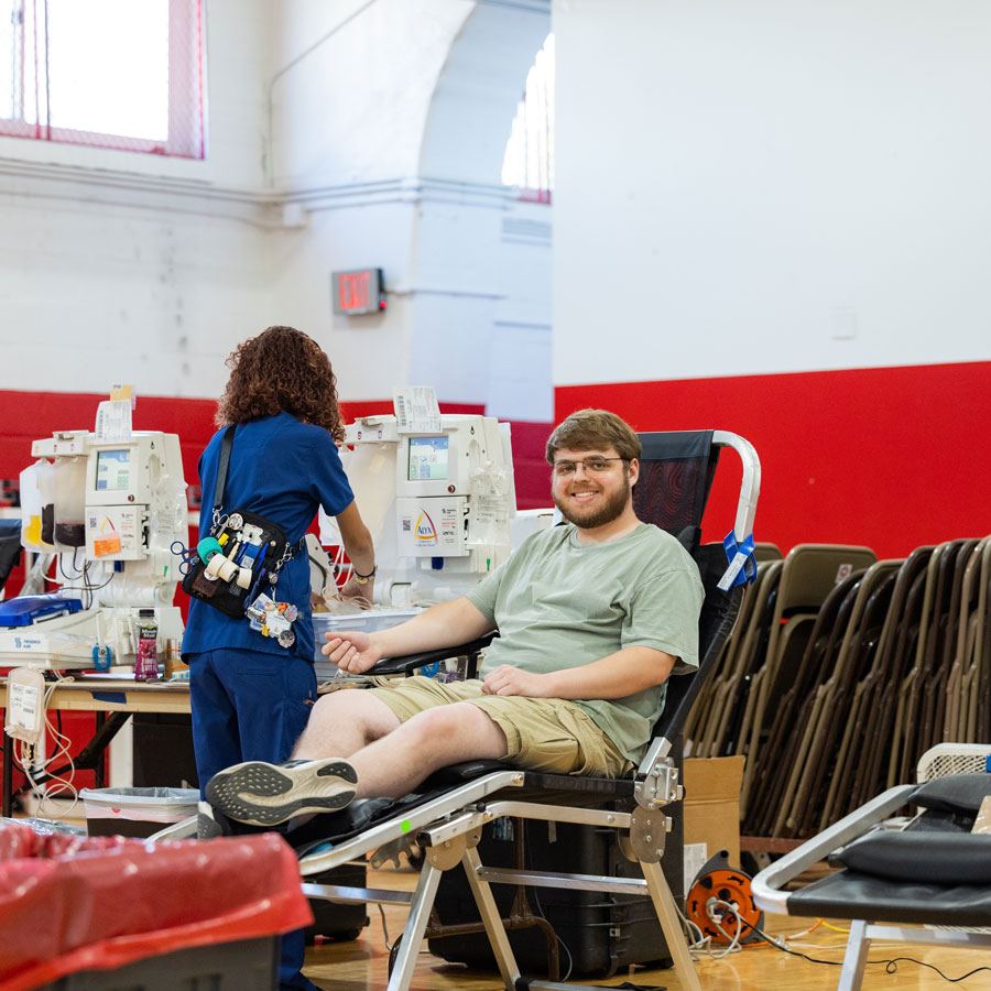 Student smiling at the camera while they give blood.
