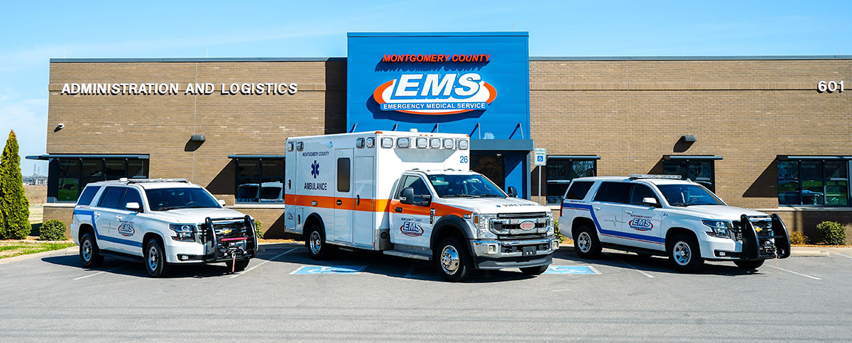 Three emergency vehicles, including an ambulance, parked in front of the Montgomery County EMS Administration and Logistics building.