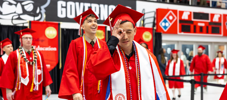 Student walking into the commencement ceremony while holding their fingers up to their eye in a monocle symbol.
