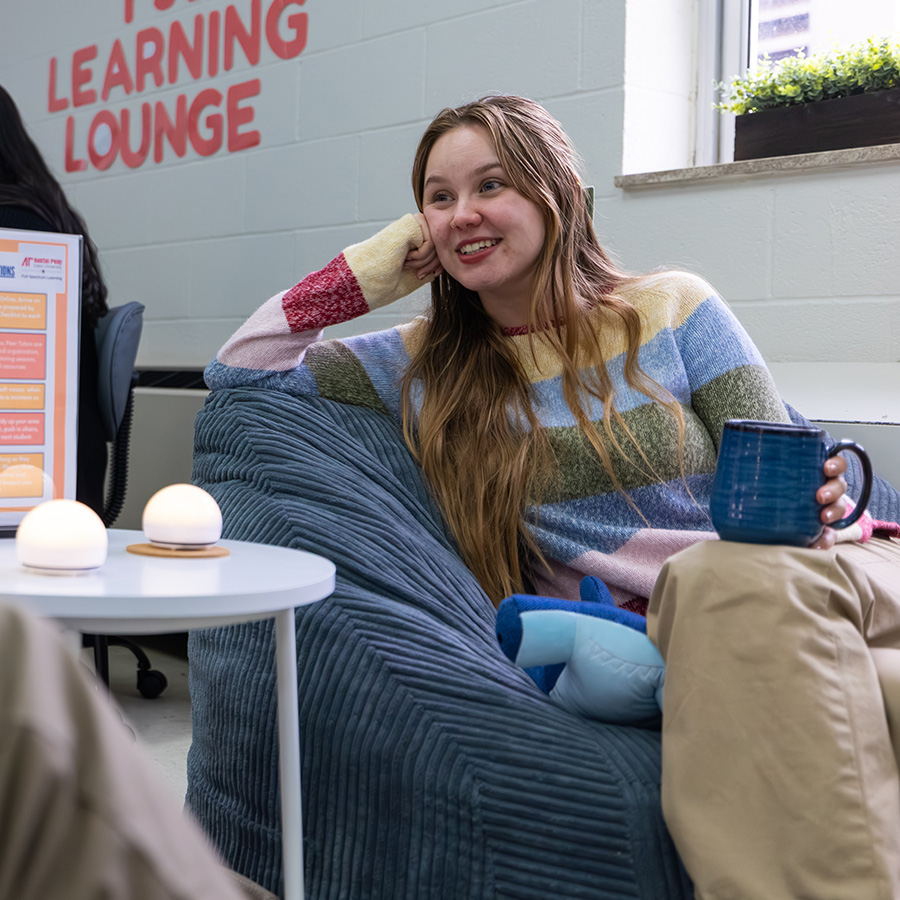 Student sitting on a beanbag chair hold a mug and hanging out in the Learning Lounge.