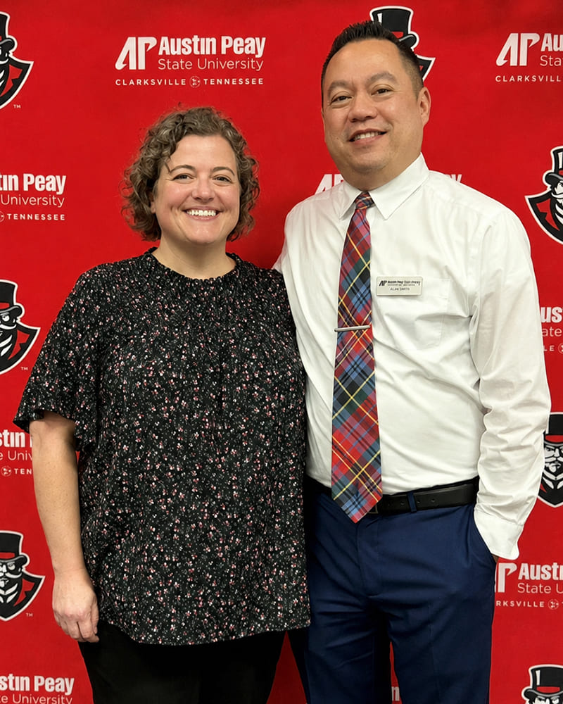 Dr. Grogan standing with Dr. McConnell infront of a red, APSU branded step-and-repeat.