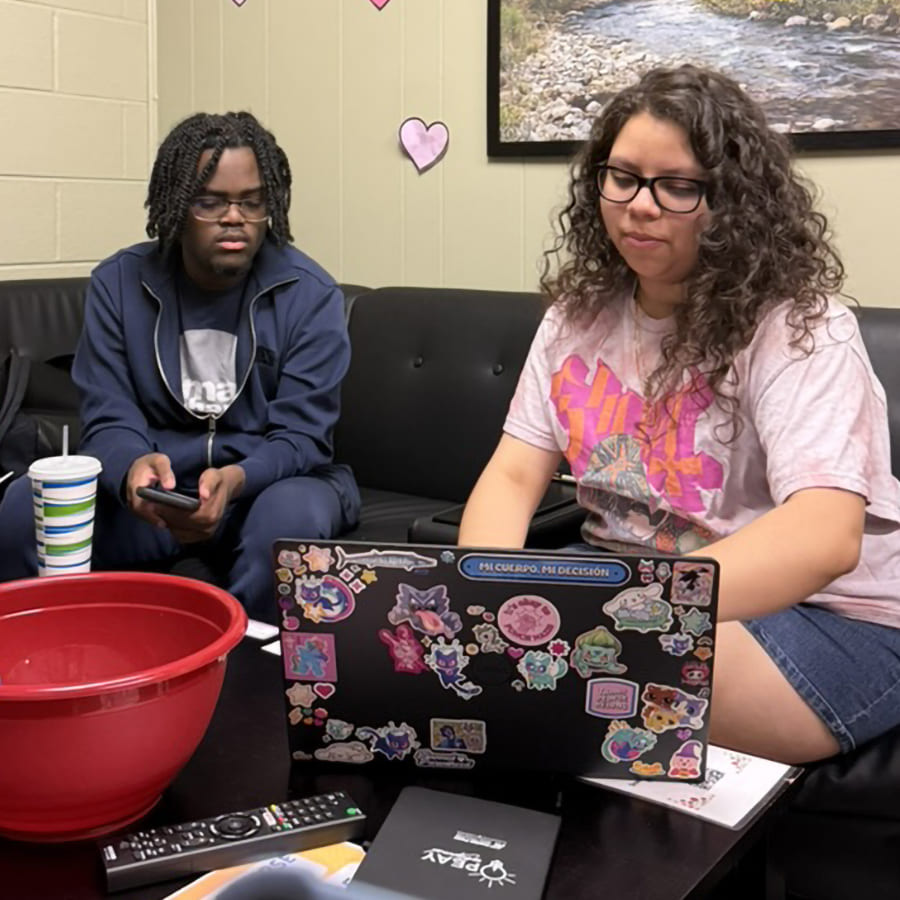 Student mentor Val and her mentee, Xavier, sitting on a couch, hard at work in front of a laptop.