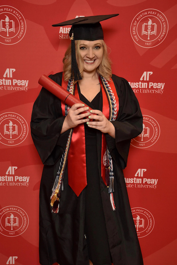 Jennifer posing with her degree tube infront of an APSU Backdrop