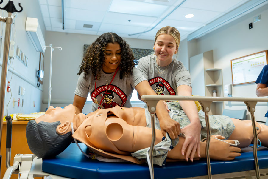 Two students practicing turning over a patients body the nursing simulation room.