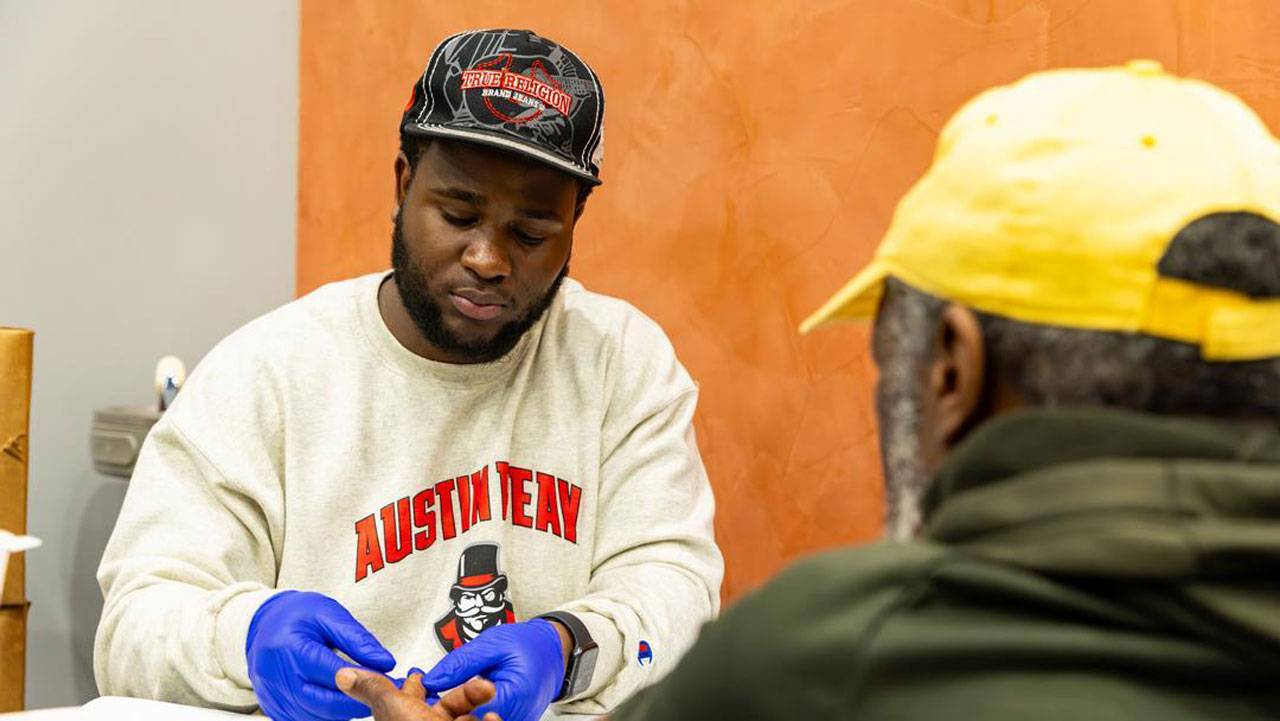 Student getting a patients finger ready to test blood sugar levels.