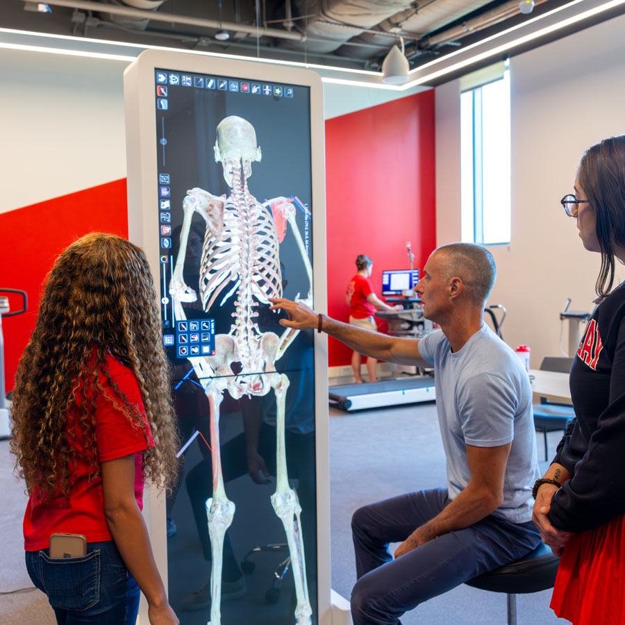 Faculty and student using new display technology in the Health Professions Building to study the bone structure of the human body.