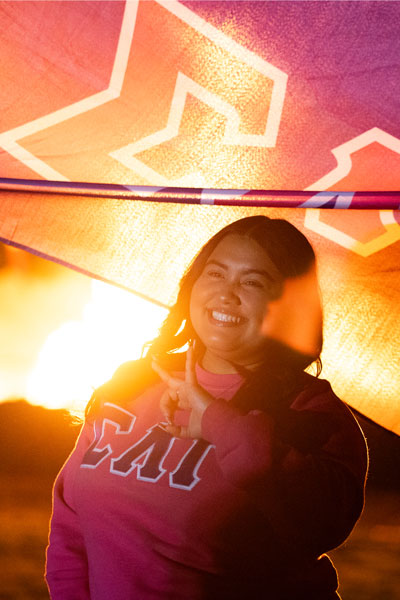 sorority member posing for a picture infront of the bonfire with their greek letters flag.