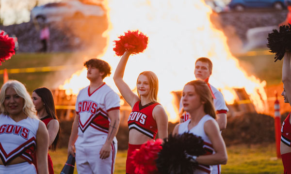 Chearleaders at the Homecoming Bonfire. The bonfire is in the background behind the cheerleaders reaching high into the sky.