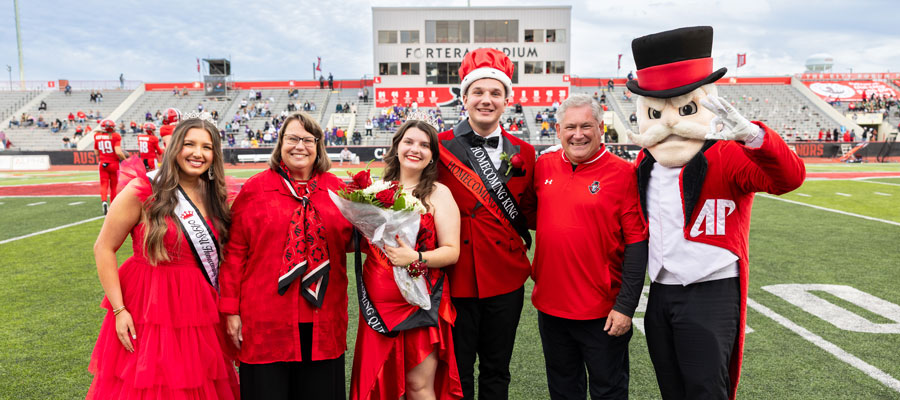 Winners of the Homecoming Court posing for a picture with previous homecoming queen, the university president and his wife, and the Gov mascot.