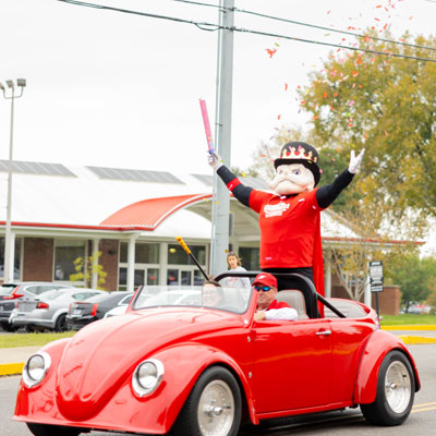 Gov mascot riding in the back of a convertable VW Beetle in the Homecoming Parade.