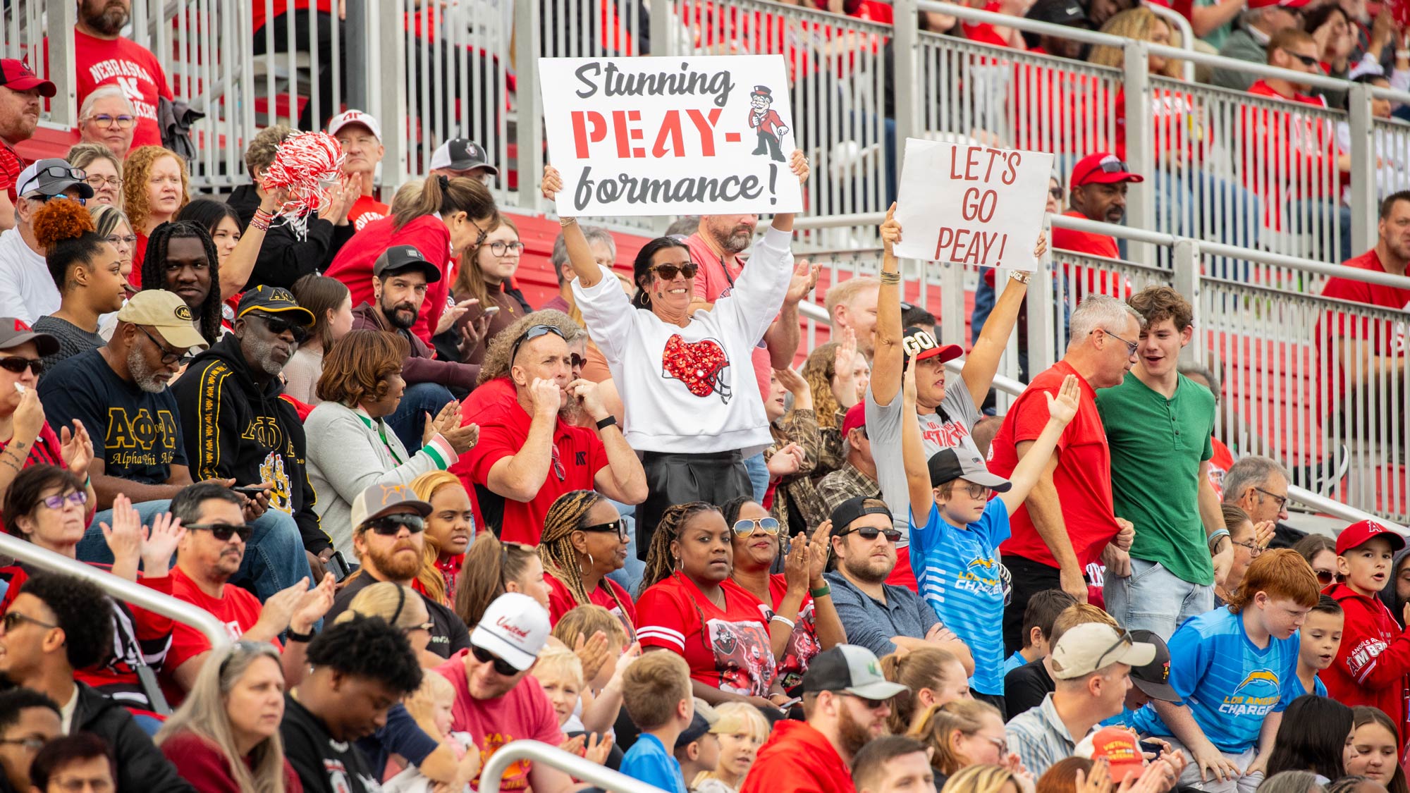 Fans in the stands holding up signs that say Lets Go Peay and Stunning PEAY formance, as they cheer on the football team.