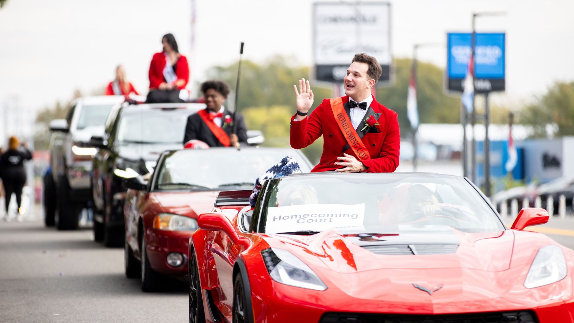Homecoming Court riding in vehicles during the parade and waving to the crowd.