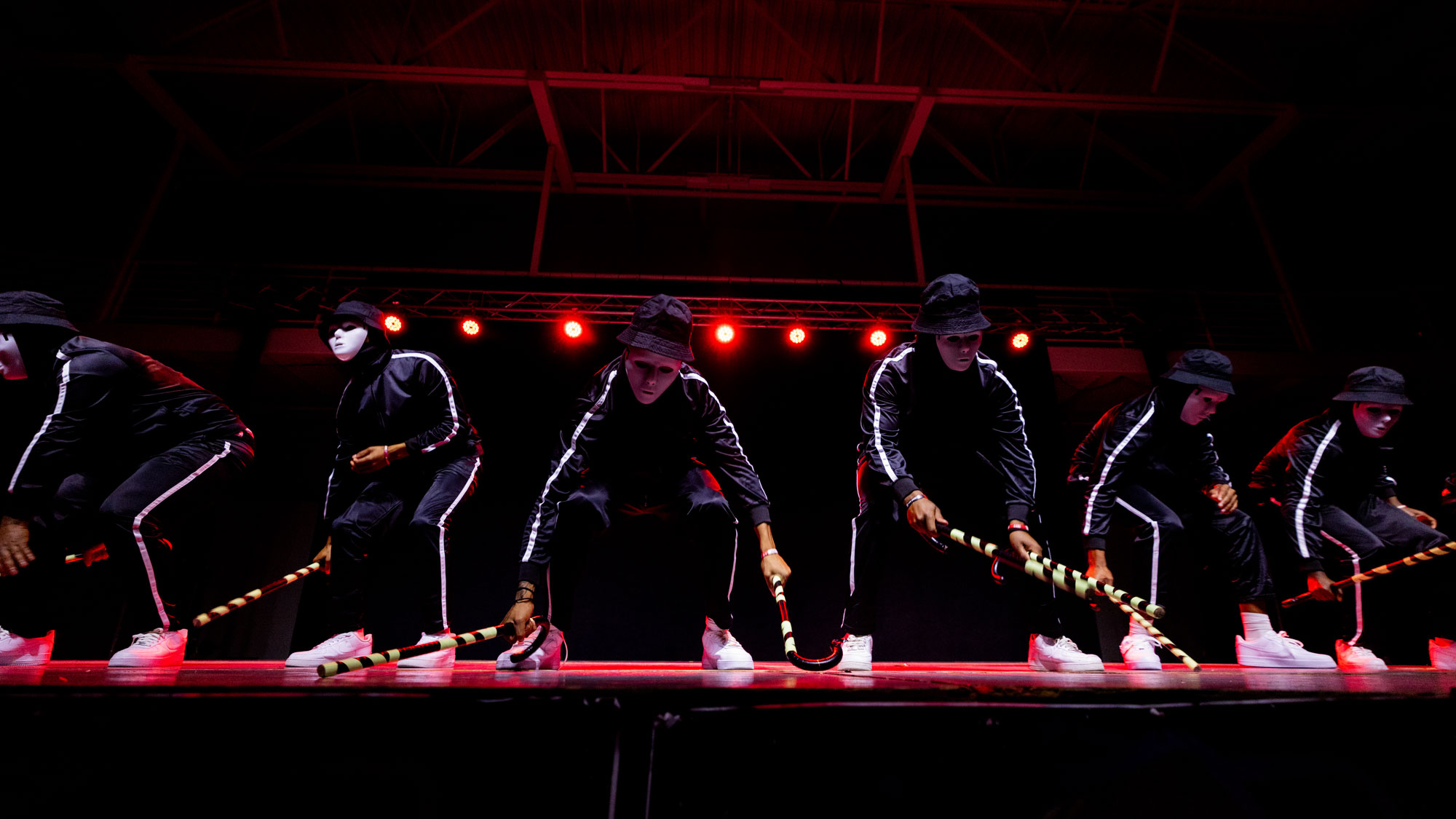 Students in back tracksuite and white blank face mask holding canes and peforming on stage during the step show.