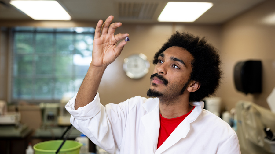 Man in a lab coat examining a small object in a laboratory