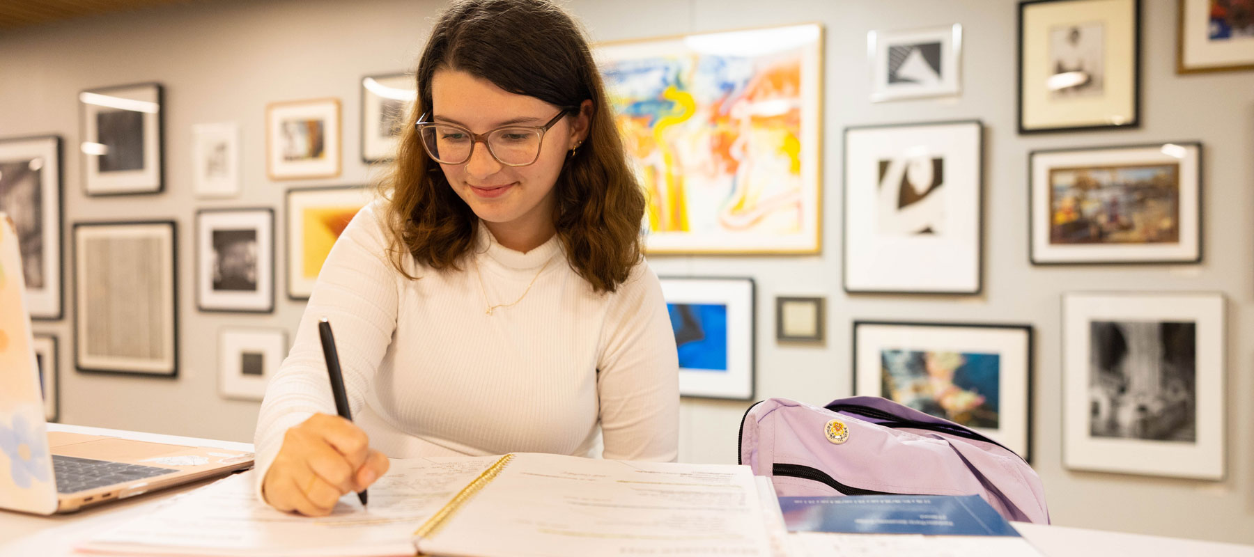 Student taking notes at a hightop table with student artwork displayed on the wall behind them.