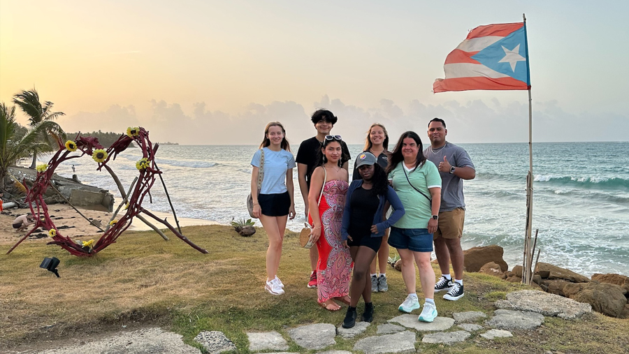 Group posing on a seaside lawn beside a Puerto Rican flag and heart-shaped floral decoration