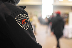 A police officer's shoulder patch in focus, in a busy indoor setting.