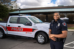 A police officer stands in front of a police truck with red and white markings.