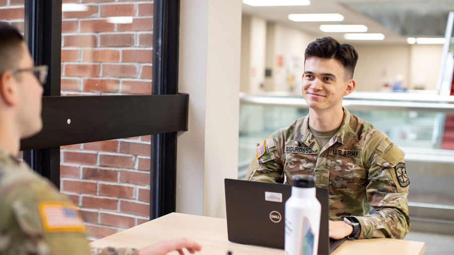 Two Students taking while one works on their laptop.