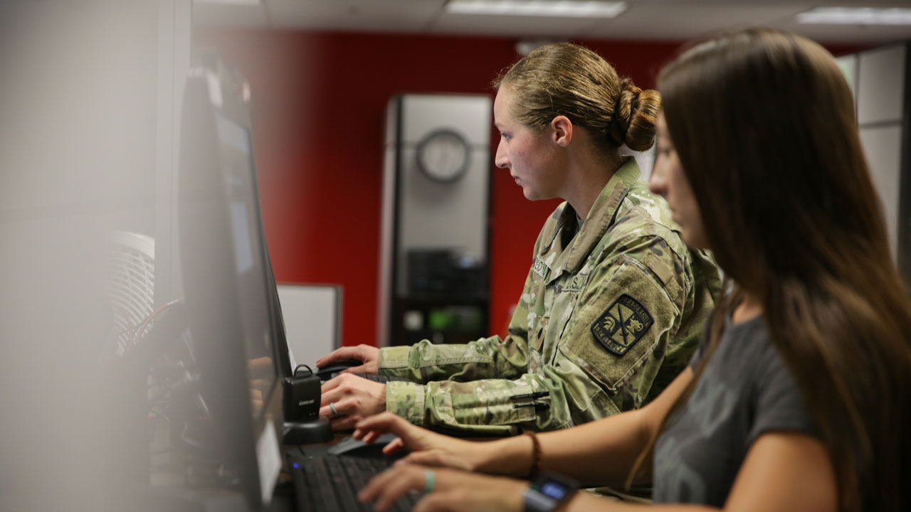 two military students working at a computer desk.
