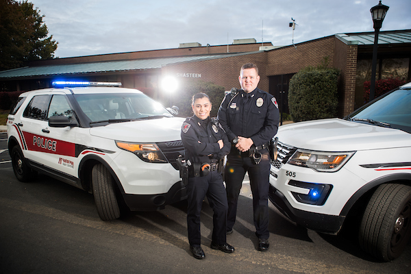 Two APSU campus police officers stand in front of their patrol vehicles.