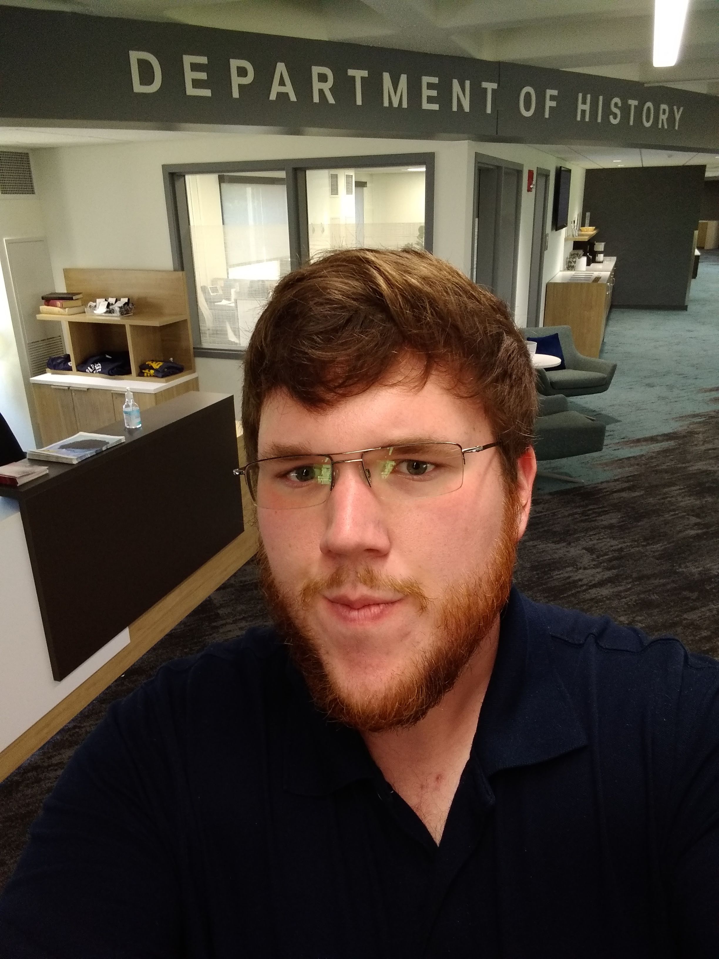 Nicholas Herrud, wearing glasses and a dark polo shirt, takes a selfie in the Austin Peay State University Department of History office.